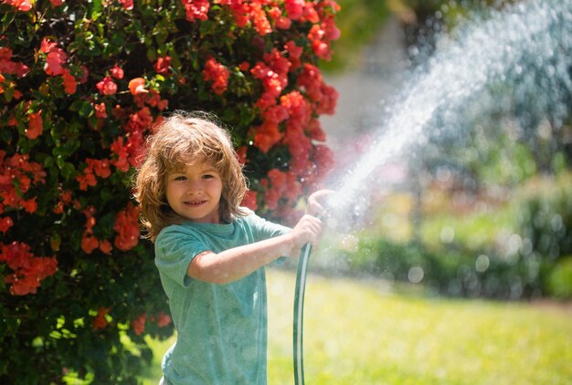 Ragazzino divertente che gioca con il tubo da giardino nel cortile di casa bambino divertendosi con spruzzi d'acqua sul cortile n