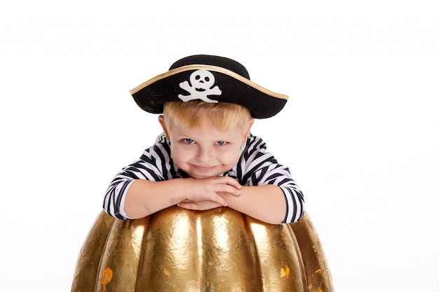 Ragazzino divertente in costumi di carnevale dei pirati che stanno con una grande zucca su bianco