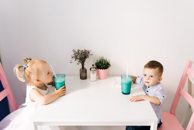 Ragazzino e ragazza alla moda in un caffè per bambini che bevono un frappè