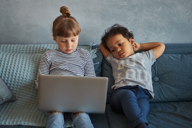 Ragazzino e ragazza che si siedono sul sofà e che giocano su un computer portatile