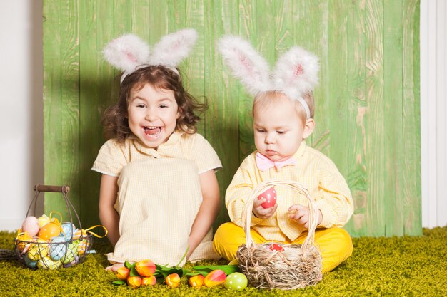 Ragazzino e ragazza come conigli di Pasqua sull'erba con uova colorate