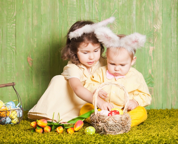 Ragazzino e ragazza come conigli di Pasqua sull'erba con uova colorate
