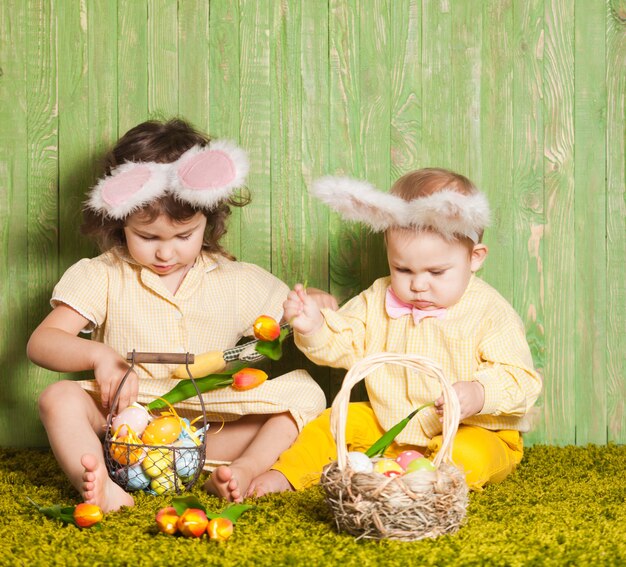 Ragazzino e ragazza come conigli di Pasqua sull'erba con uova colorate