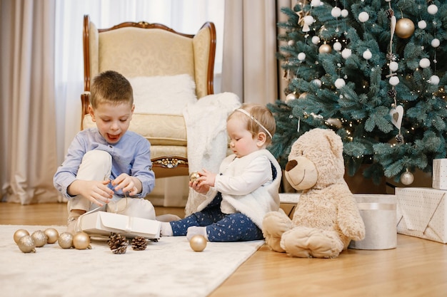 Ragazzino e sua sorella seduti vicino all'albero di Natale a casa