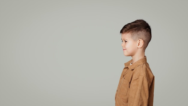 Ragazzino europeo sorridente che guarda lo spazio vuoto isolato sul panorama grigio dello sfondo dello studio