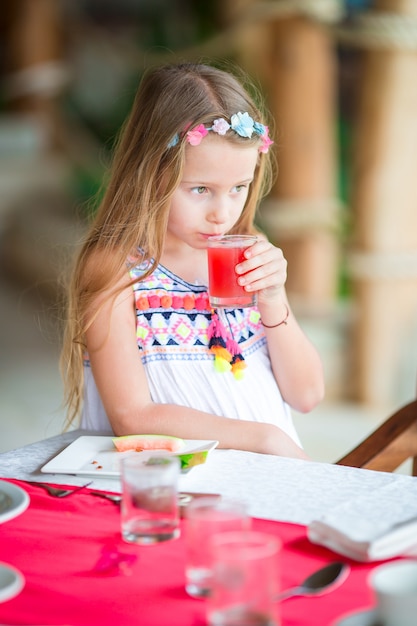 Ragazzino facendo colazione al caffè all'aperto. Ragazza adorabile che beve il succo di anguria fresco che gode della prima colazione.