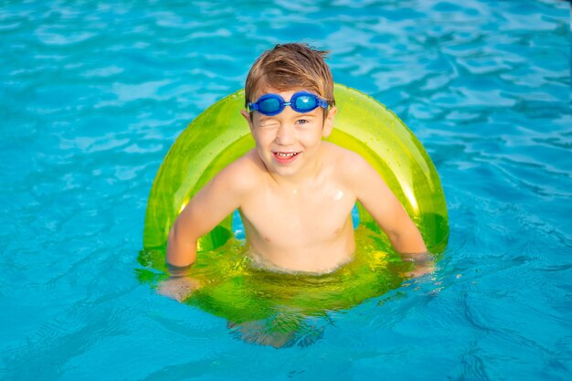 Ragazzino felice bambino nuota in piscina su un cerchio gonfiabile di gomma in estate estate weekend per bambini vacanza per bambini bambino nel parco acquatico