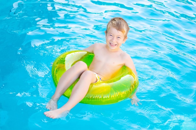 Ragazzino felice bambino nuota in piscina su un cerchio gonfiabile di gomma in estate estate weekend per bambini vacanza per bambini bambino nel parco acquatico