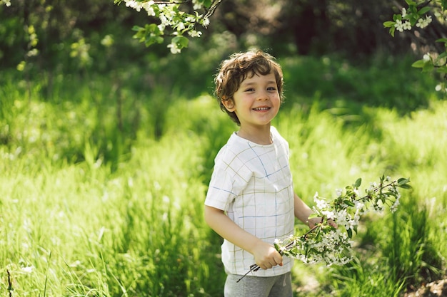 Ragazzino felice che cammina nel giardino primaverile Bambino che gioca con il ramo di un ciliegio e si diverte Bambino che esplora la natura Bambino che si diverte Attività primaverile per bambini curiosi