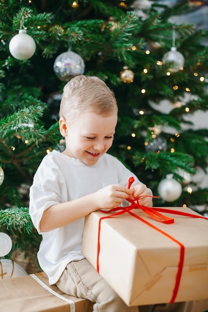 Ragazzino felice che disimballa un contenitore di regalo vicino all'albero di Natale