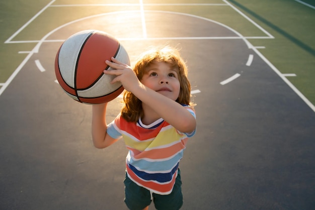 Ragazzino felice che gioca a basket nello sport del parco giochi per bambini
