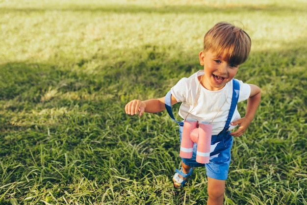 Ragazzino felice che gioca con un binocolo alla ricerca di un'immaginazione o di un'esplorazione in una giornata estiva nel parco Bambino attivo che gioca e corre sull'erba verde all'aperto Concetto di infanzia