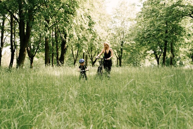 Ragazzino felice che guida una bicicletta con una giovane mamma nel parco
