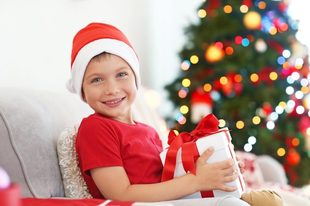 Ragazzino felice con scatola regalo di Natale seduto sul divano di casa