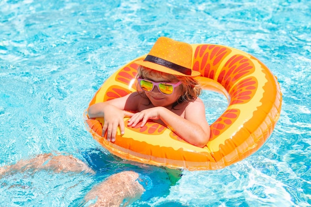 Ragazzino felice del cocktail dei bambini di estate con l'anello gonfiabile variopinto nella piscina all'aperto su summ