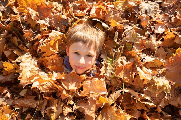 Ragazzino felice in un mucchio di foglie gialle nel parco autunnale