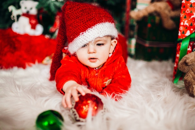 Ragazzino grazioso in vestito rosso prima di un albero di Natale