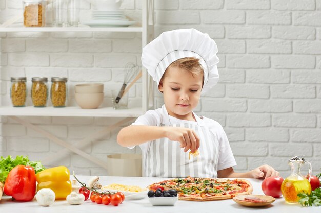 Ragazzino in cappello da chef e un grembiule che cucina la pizza