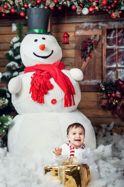 Ragazzino in costume pupazzo di neve seduto in un interno di casa dal grande pupazzo di neve e in attesa di Babbo Natale