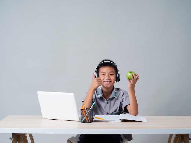 Ragazzino in cuffie che studiano in linea facendo uso del computer portatile