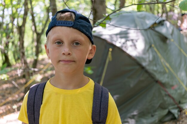 Ragazzino in un cappello vicino alla tenda all'aperto. Campo estivo