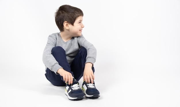 Ragazzino in una felpa grigia pantaloni della tuta blu e scarpe da ginnastica su sfondo bianco