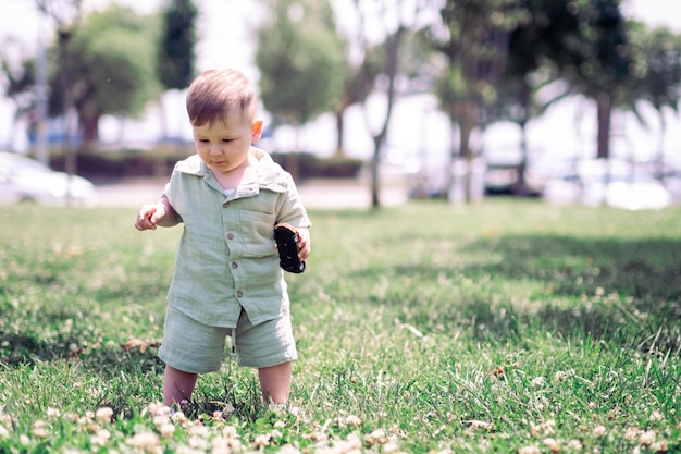 ragazzino in vestito di cotone che tiene l'auto giocattolo in piedi sul prato verde con fiori nel parco urbano estivo