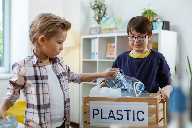 Ragazzino premuroso. Ragazzini laboriosi che riempiono il fagiolo della spazzatura con immondizia di plastica mentre praticano la lezione