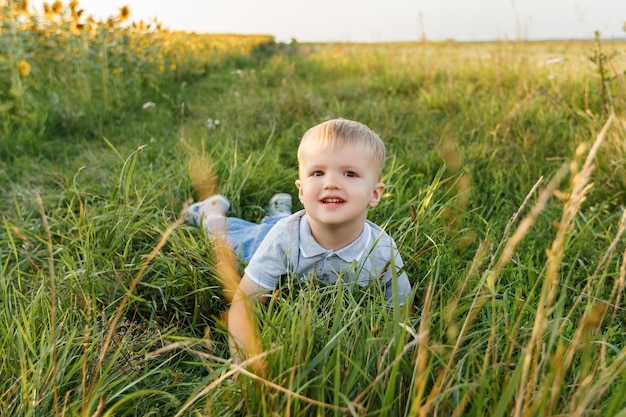 Ragazzino sdraiato sull'erba e sorridente Bambino di tre anni che si diverte in campo al tramonto