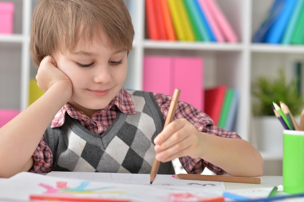 Ragazzino seduto a tavola e disegna con matite colorate