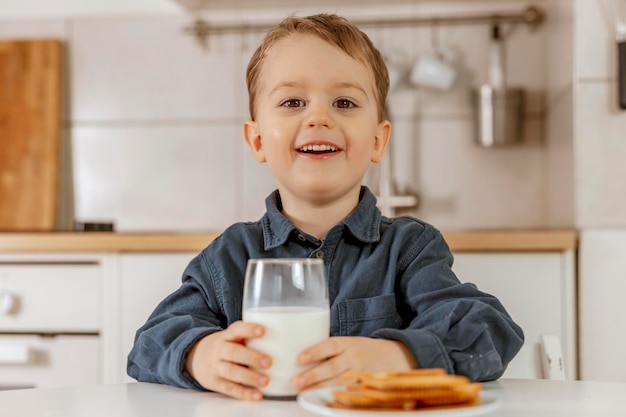 Ragazzino seduto in cucina e bere latte Latte fresco in latticini di vetro bevanda salutare Fonte sanitaria di lattosio di calcio Interni accoglienti e moderni Bambino in età prescolare con abbigliamento casual