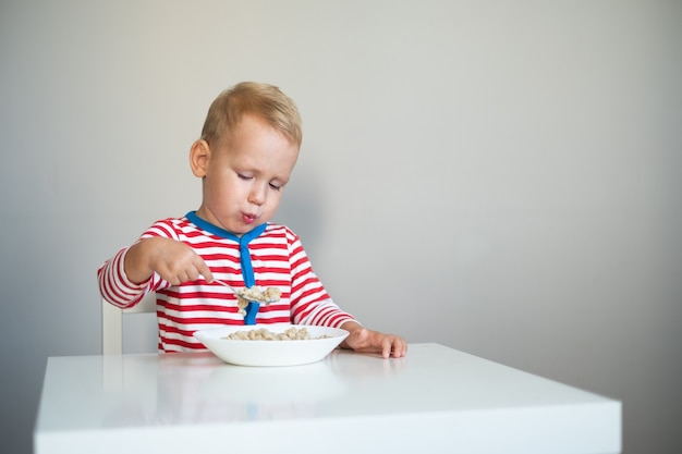 ragazzino si siede a tavola e mangia farina d'avena con un cucchiaio grande