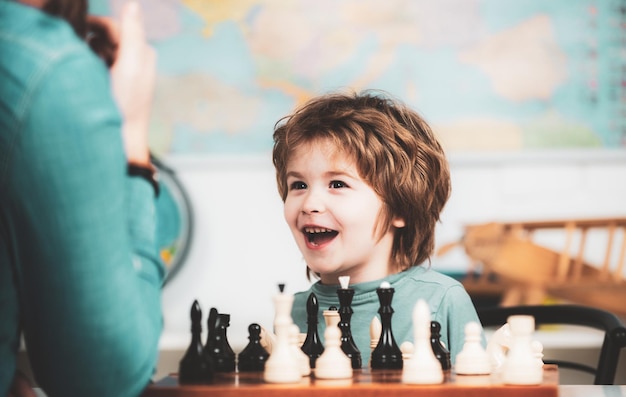 Ragazzino sorridente allegro della scuola di scacchi del bambino che si siede al tavolo e che rivela gioia mentre gioca