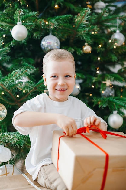 Ragazzino sorridente che disimballa un contenitore di regalo vicino all'albero di Natale