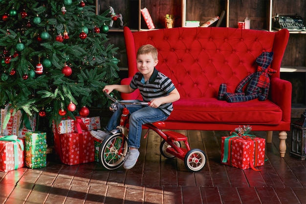 Ragazzino sorridente che guida la bicicletta nella stanza con l'albero di natale