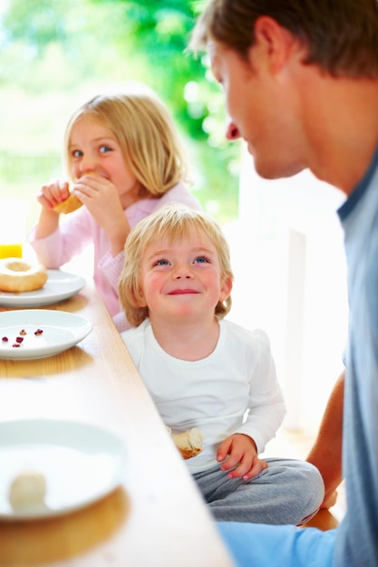Ragazzino sorridente con suo padre e sua sorella che fanno colazione Ritratto di un ragazzino sorridente con suo padre e sua sorella che fanno colazione