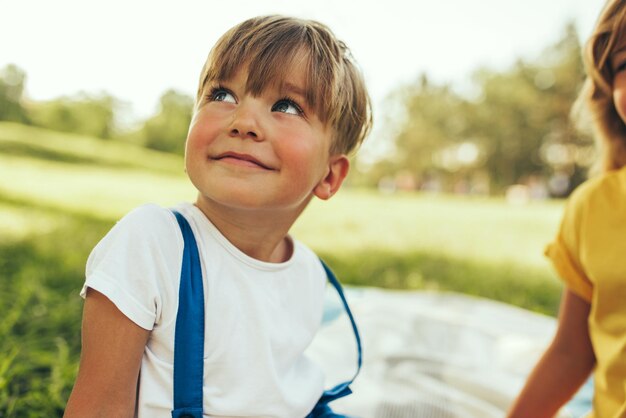 Ragazzino sorridente seduto sulla coperta sullo sfondo della natura Bambino felice che si gode l'estate con sua sorella nel parco Bambino bello che sorride e si diverte alla luce del sole all'aperto Infanzia