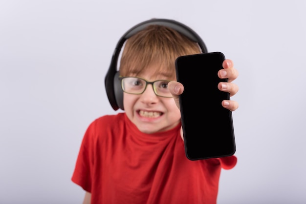 Ragazzino spaventato con le cuffie che tengono smartphone con schermo nero vuoto Il bambino ha rotto il telefono Copia spazio Mockup