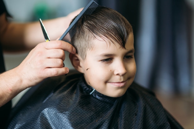 Ragazzino su un taglio di capelli nel barbiere si siede su una sedia.