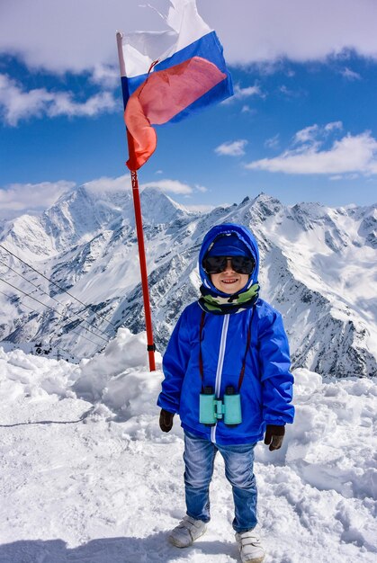 Ragazzino sullo sfondo delle montagne innevate e la bandiera della Russia Elbrus Russia 2019