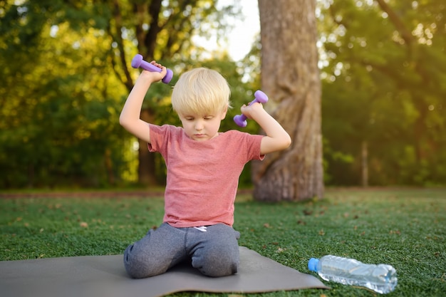 Ragazzino sveglio che alza i dumbbells all&#39;aperto