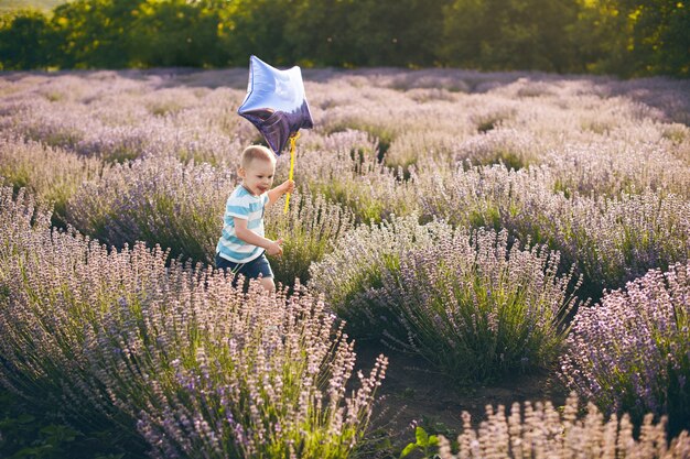 Ragazzino sveglio che funziona nel campo del fiore all'aperto che tiene un palloncino.