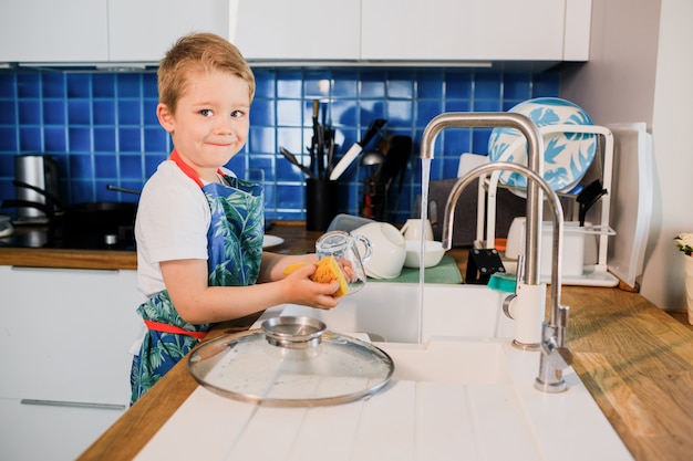 Ragazzino sveglio che lava i piatti nella cucina