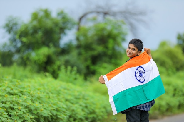 Ragazzino sveglio che ondeggia la bandiera tricolore nazionale indiana sopra il fondo della natura