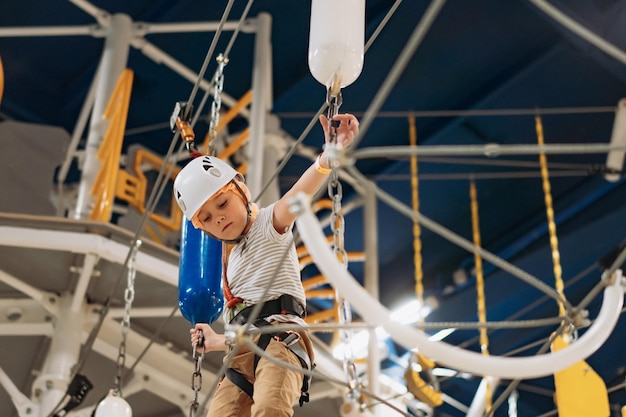 Ragazzino sveglio che si arrampica nel parco avventura che passa il parco ad alta fune della corsa ad ostacoli all'interno