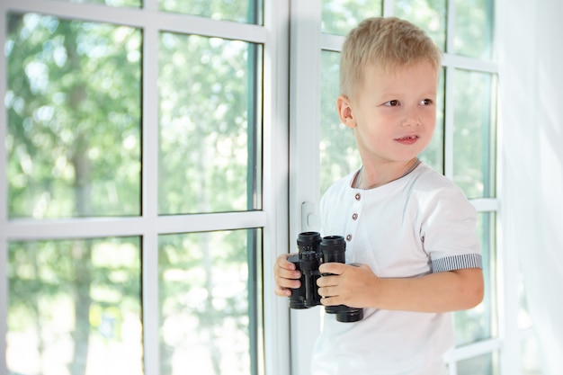 Ragazzino sveglio che tiene binocolo nero e distoglie lo sguardo dalla fotocamera.