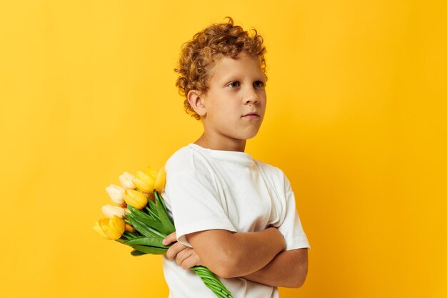 Ragazzino sveglio con i fiori gialli che posano il fondo giallo di divertimento dell'infanzia inalterato