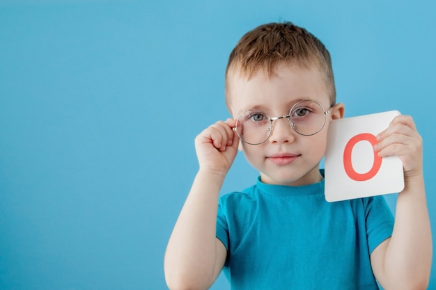 Ragazzino sveglio con la lettera sulla parete blu. Bambino che impara a lettere. Alfabeto