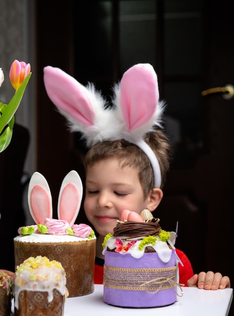 Ragazzino sveglio con le orecchie del coniglietto che guarda la gustosa torta dolce di pasqua