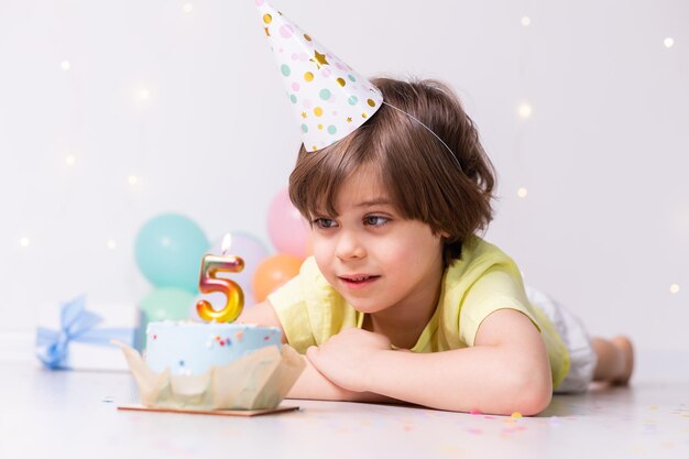 Ragazzino sveglio di compleanno in torta di cappello con candela cinque palloncini buon compleanno